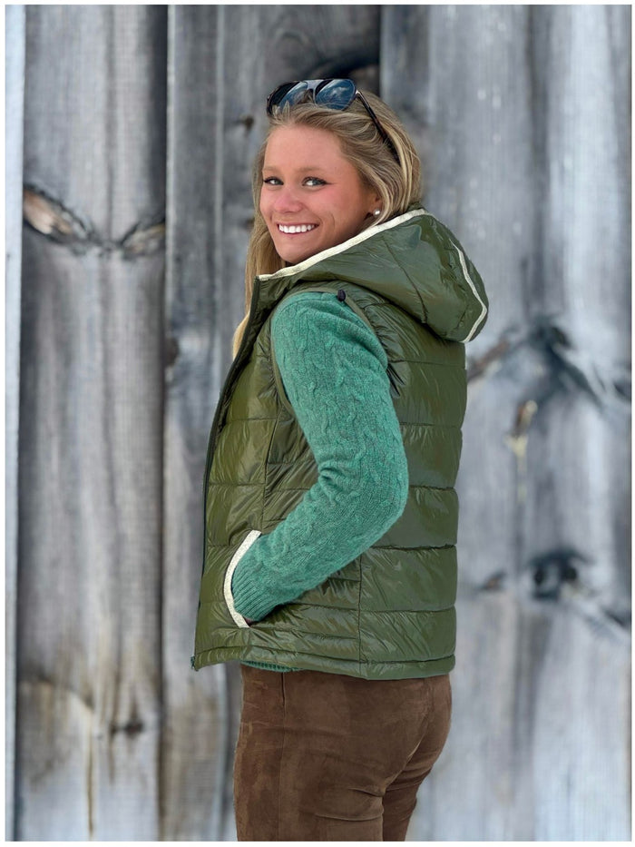Woman wearing a green puffer vest over a green sweater against a wooden background